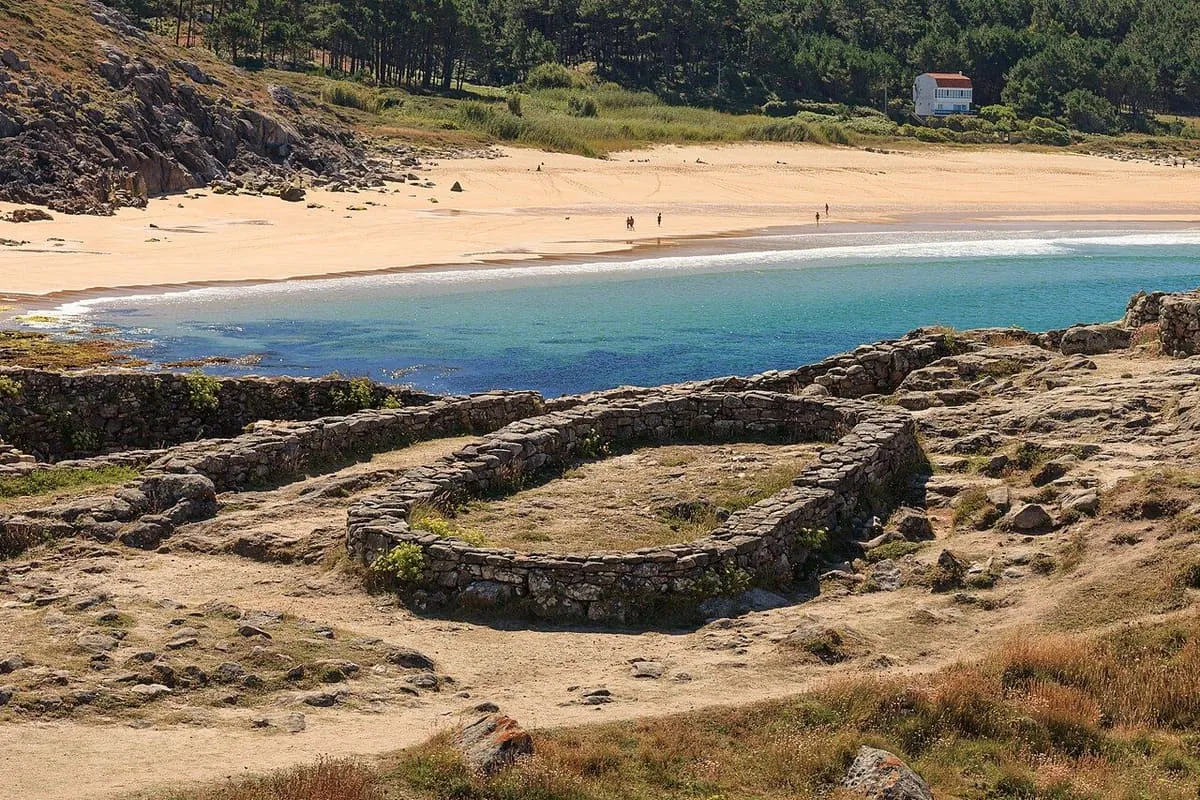 Una casa circular del castro en primer plano y la playa de Areia Longa detrás