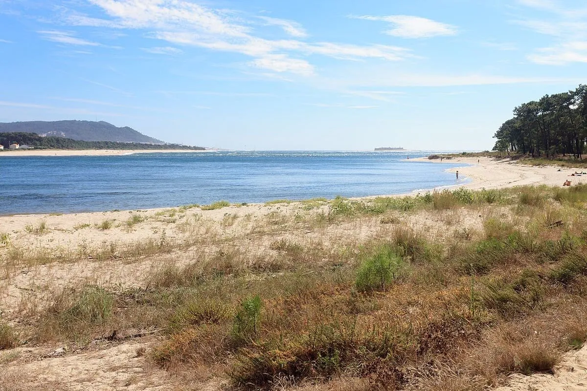 La playa de O Muíño, con dunas y vegetación junto a la desembocadura del Miño y la costa portuguesa al fondo