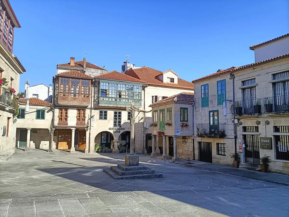 Plaza con soportales, casas de piedra con galerías y un crucero en el centro