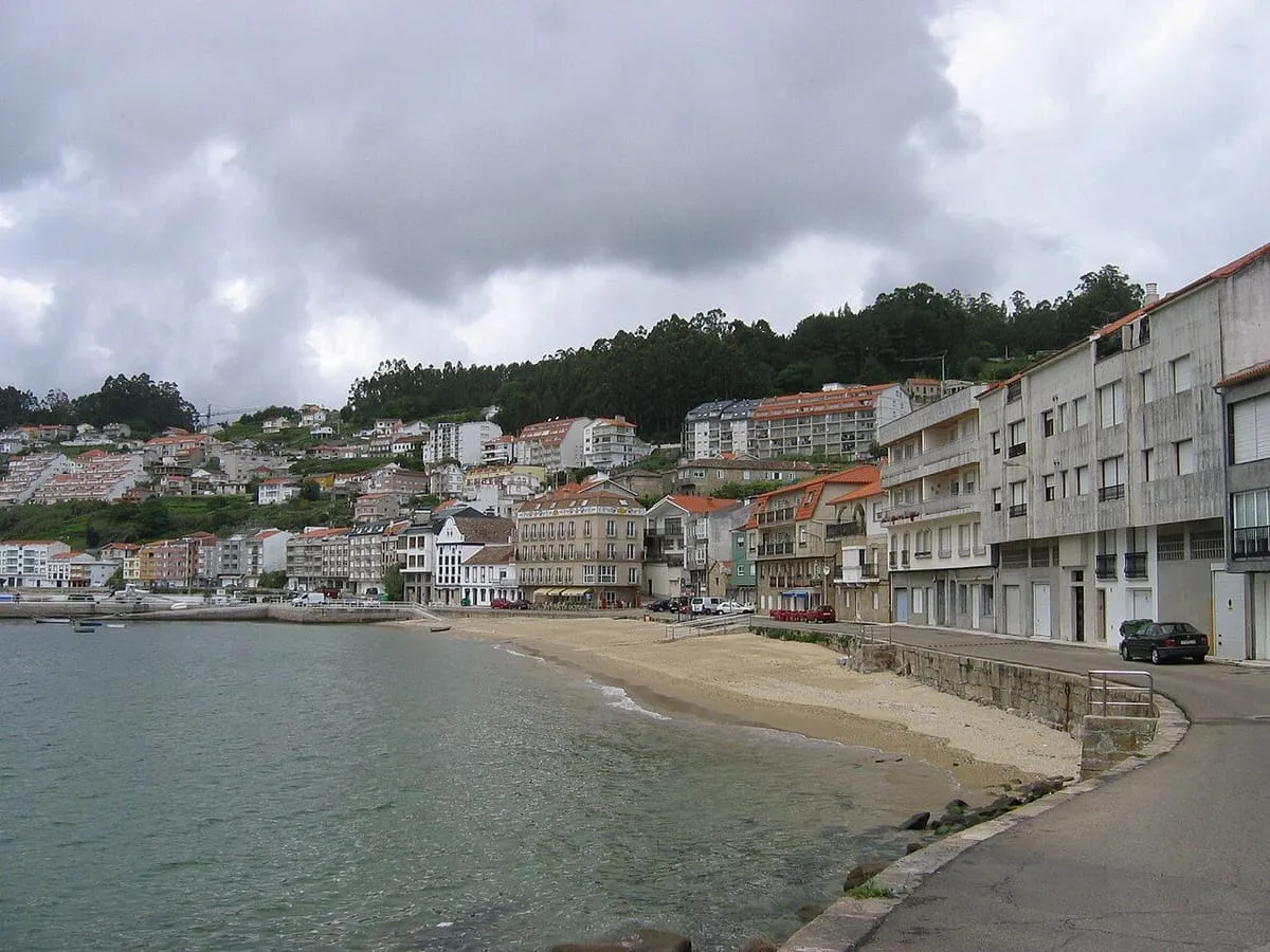 Playa de arena y casas del pueblo marinero de Raxó, con el monte detrás