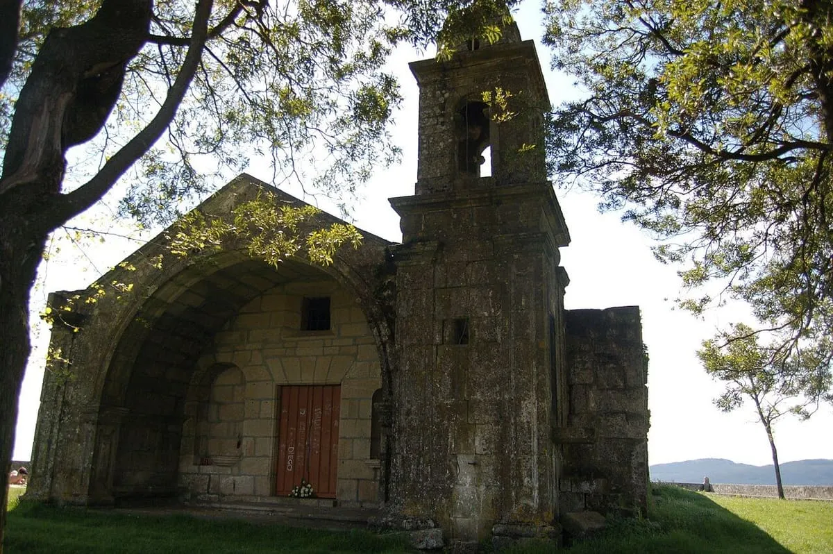 Fachada de la capela da Virxe das Neves bajo árboles, con su campanario