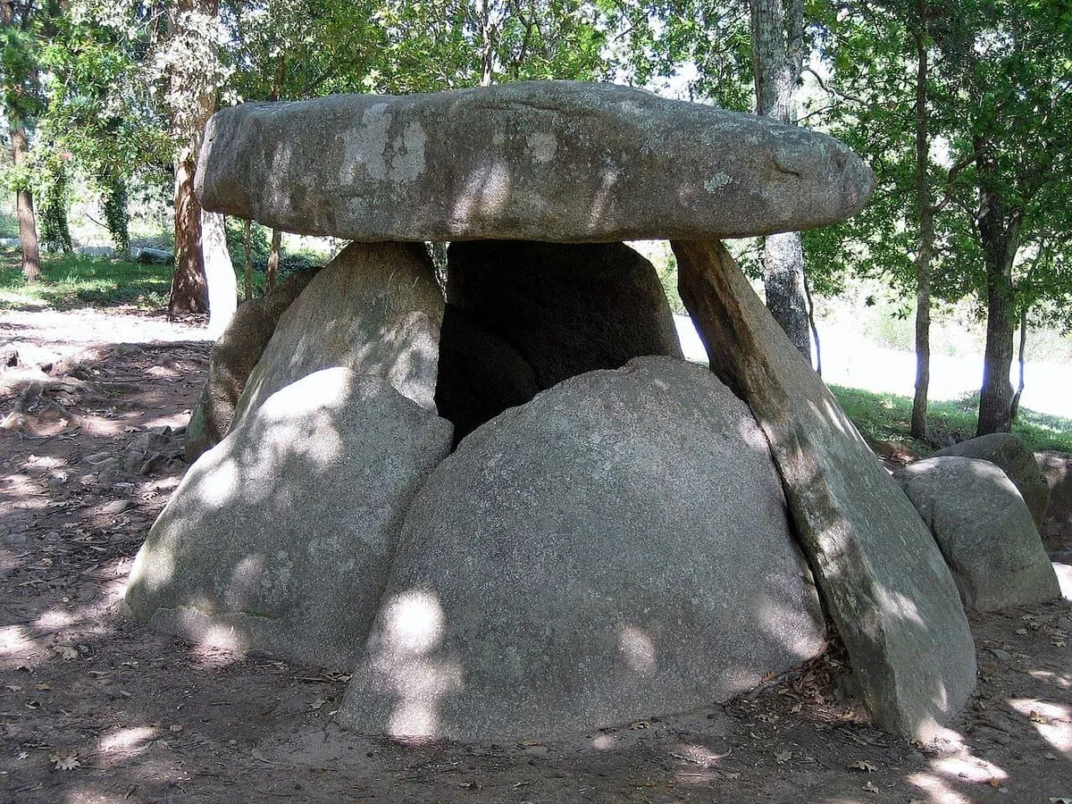 El dolmen de Axeitos en su claro del bosque, con sol entre los árboles