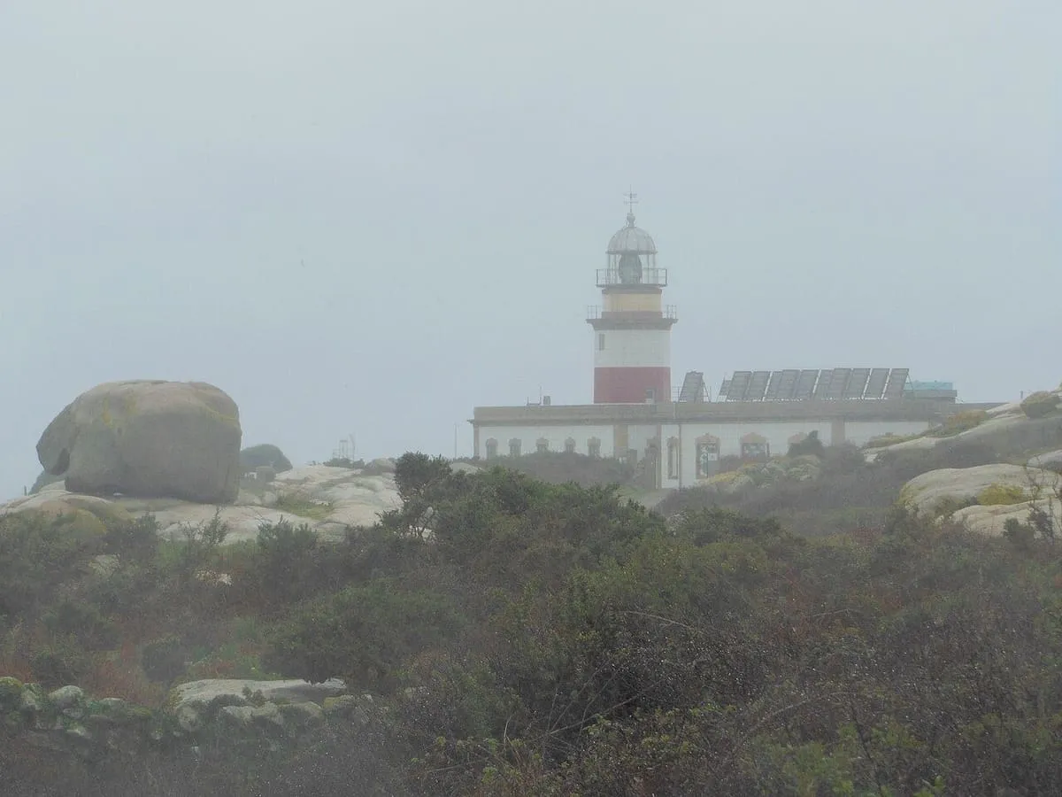 El faro de Sálvora, con su torre blanca y rojiza, entre rocas de granito en un día de niebla