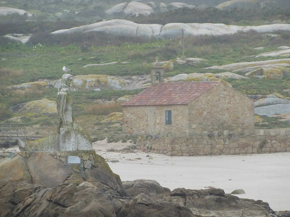 La escultura de la sirena sobre las rocas de la costa de Sálvora, con la capilla al fondo