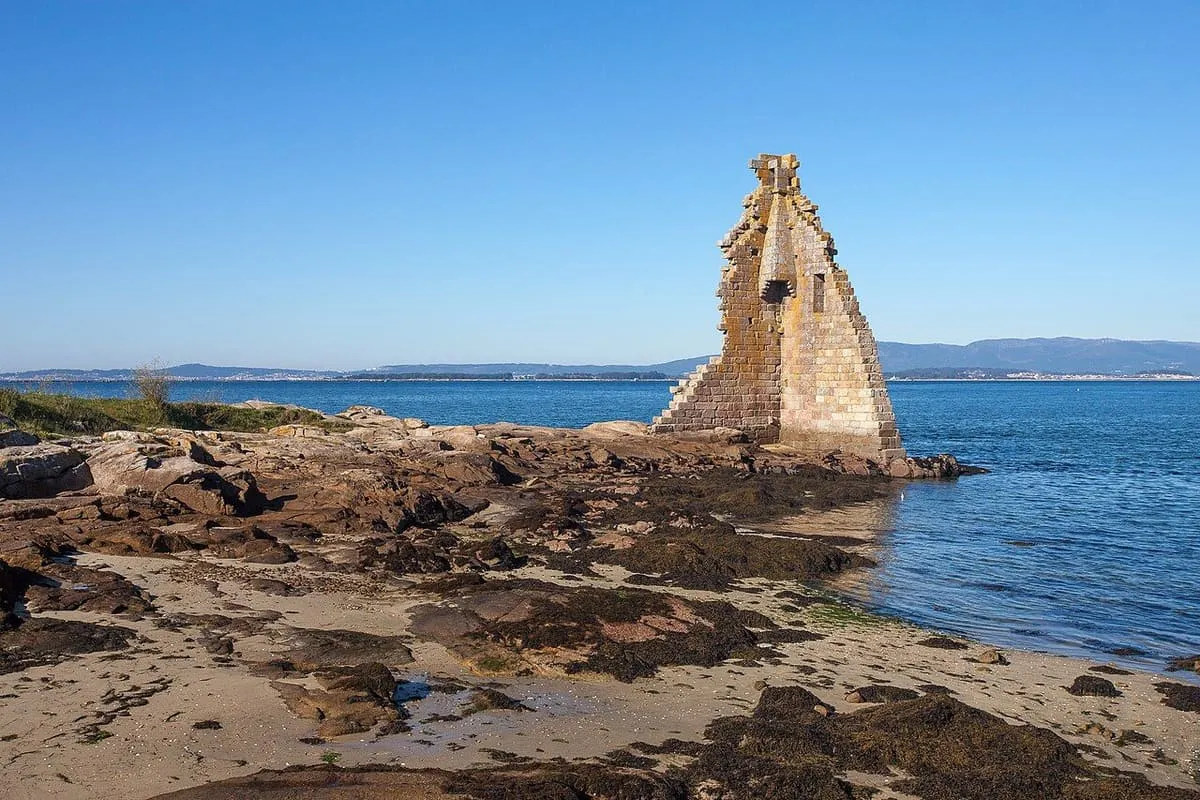 Rocas cubiertas de algas junto a la torre en ruinas, con la ría al fondo