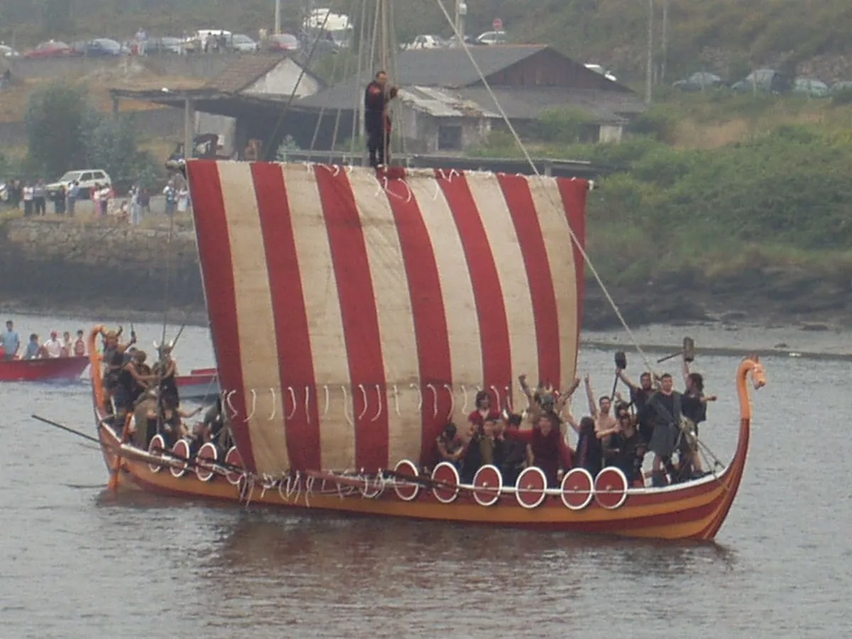Barco vikingo de vela a rayas rojas y blancas, con remeros en el río, durante la romería de Catoira