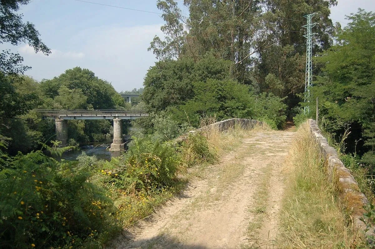 La calzada de la antigua ponte da Fillaboa entre muretes, con puentes modernos al fondo sobre el Tea
