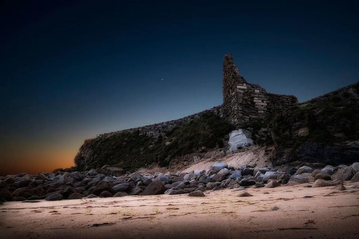 Silueta del castillo de la Lanzada sobre las rocas al atardecer, con el cielo azul oscuro
