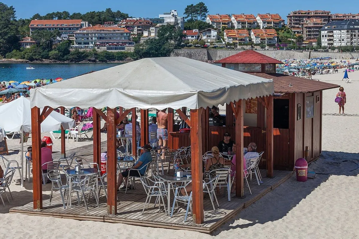 Terraza de madera con sombrilla en la arena de Silgar, con la bahía al fondo