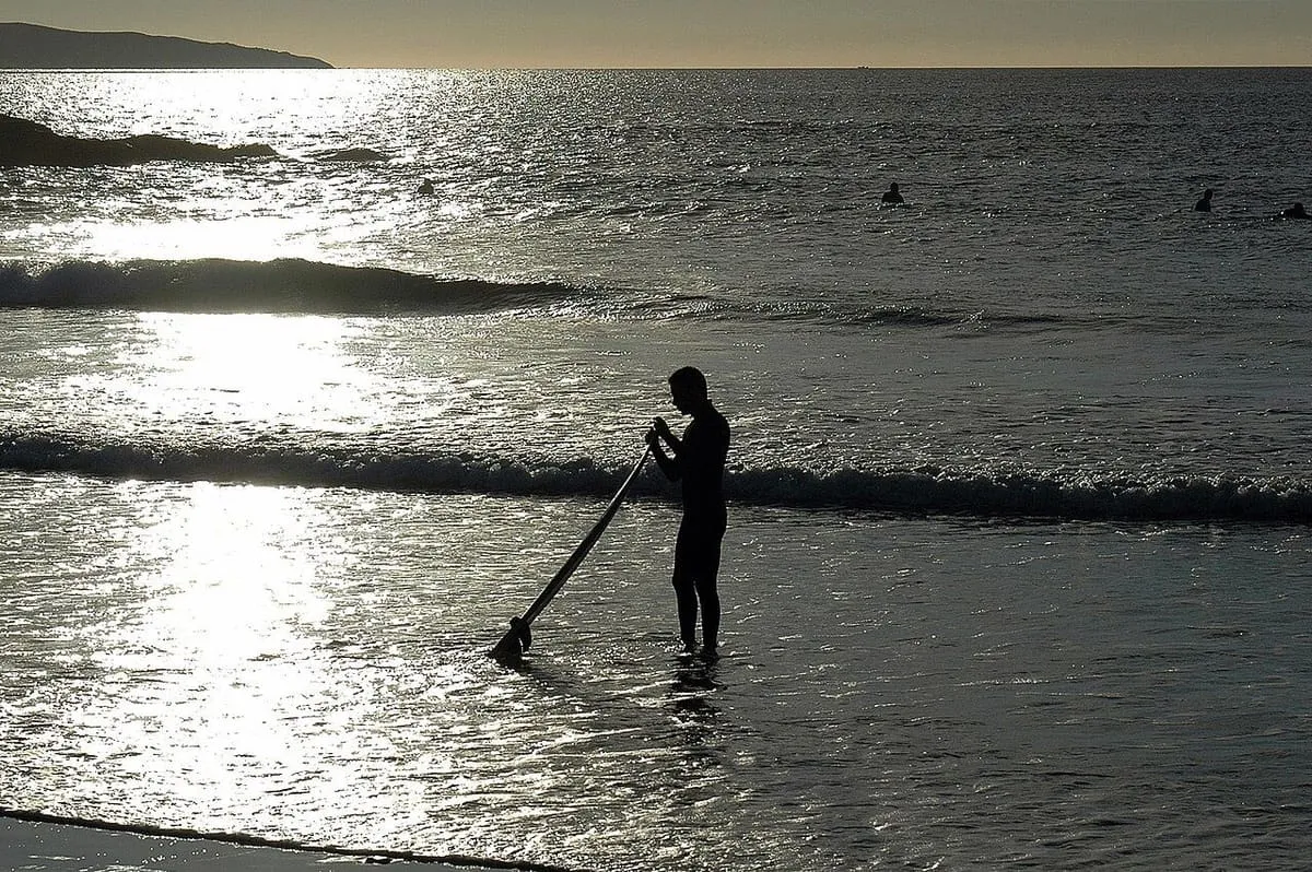 Surfista a contraluz con su tabla entrando al agua en la playa de A Lanzada