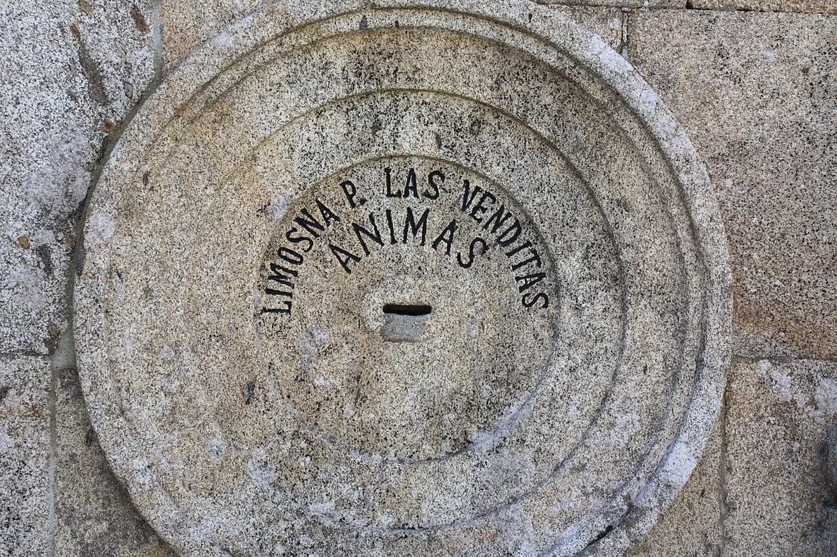 Una piedra circular con la inscripción «Limosna p. las benditas ánimas» y una ranura para monedas