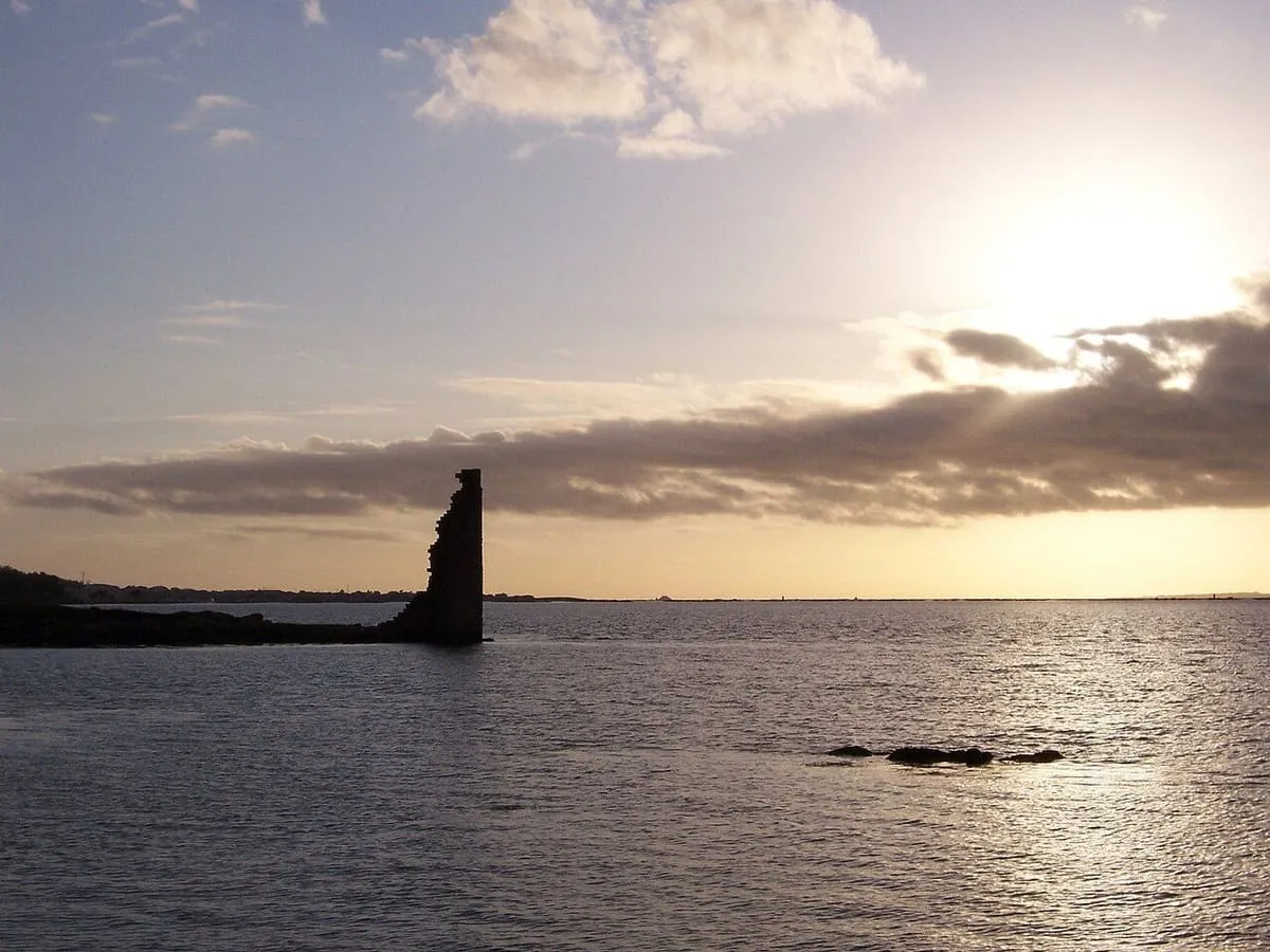 Silueta oscura de la torre sobre el agua, con el sol entre nubes