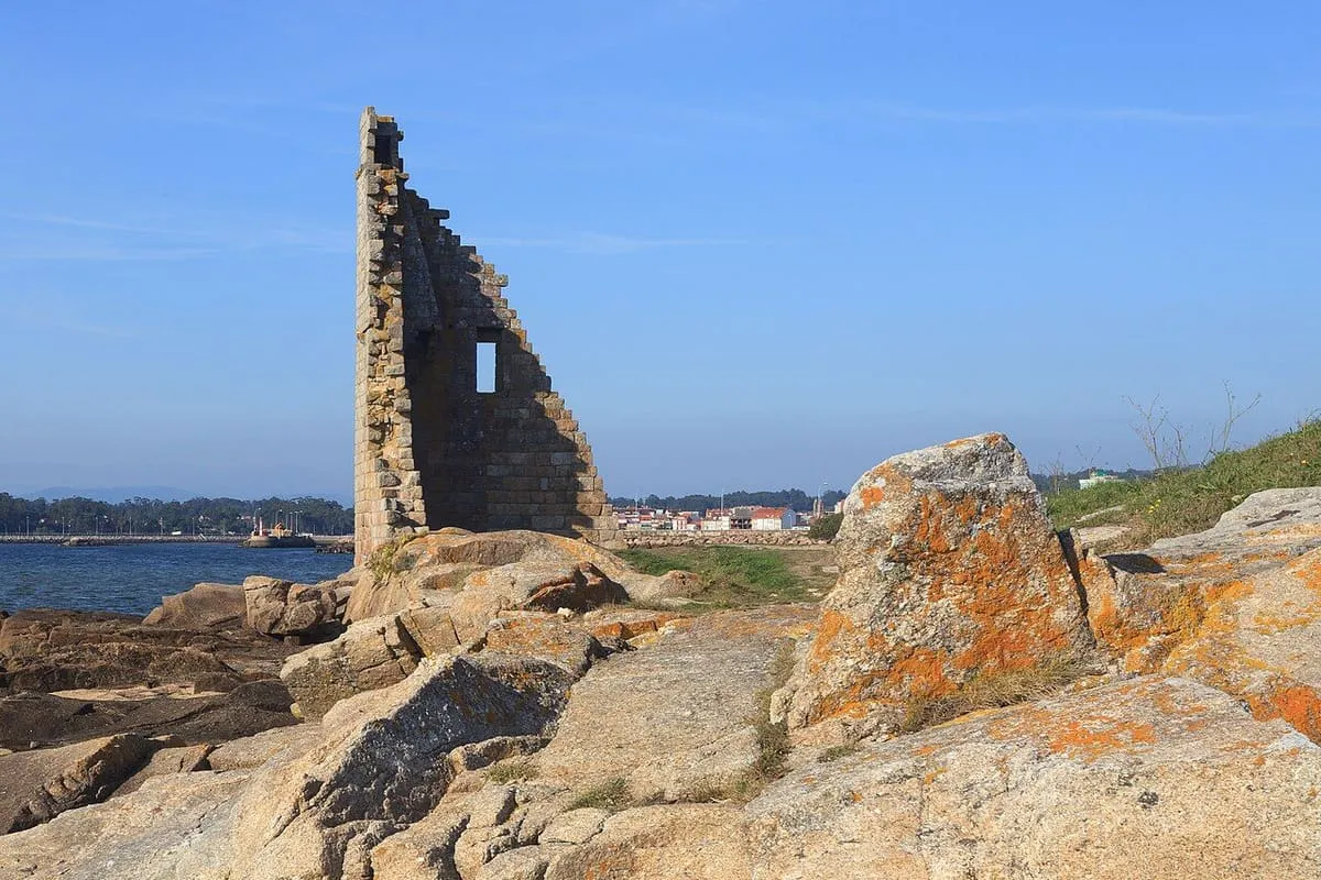 Bloques de granito con líquenes naranjas en primer plano y la torre de San Sadurniño detrás