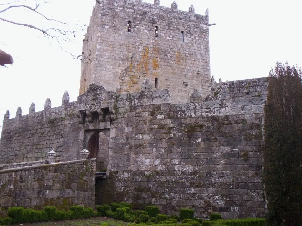 Torre del homenaje almenada y muralla de piedra del castillo de Soutomaior, con setos recortados al pie