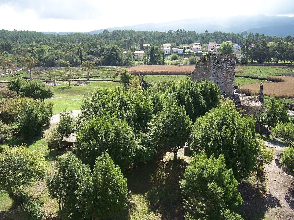 Una de las torres entre árboles y prados, con las marismas y las casas de Catoira al fondo