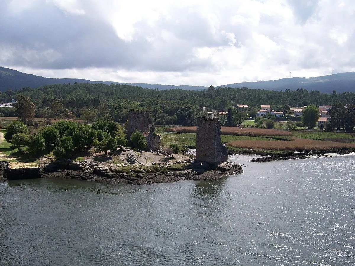 Las dos torres de piedra sobre una pequeña isla rocosa del río Ulla, con Catoira al fondo