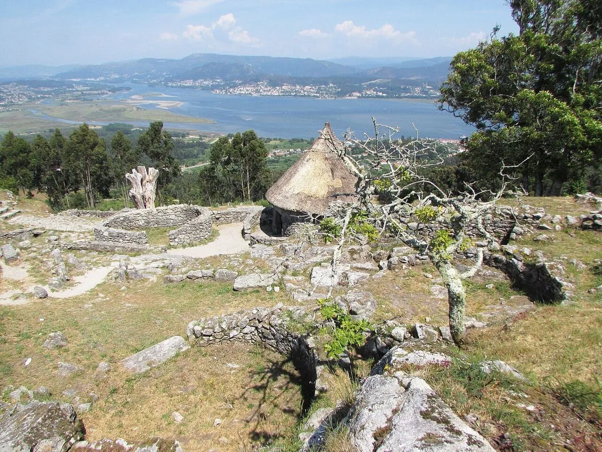 Restos del castro con una casa circular de paja y el estuario del Miño al fondo
