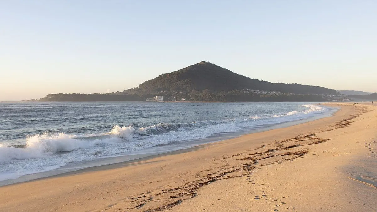 El monte Santa Trega visto desde una playa de Portugal, con olas en la orilla al atardecer