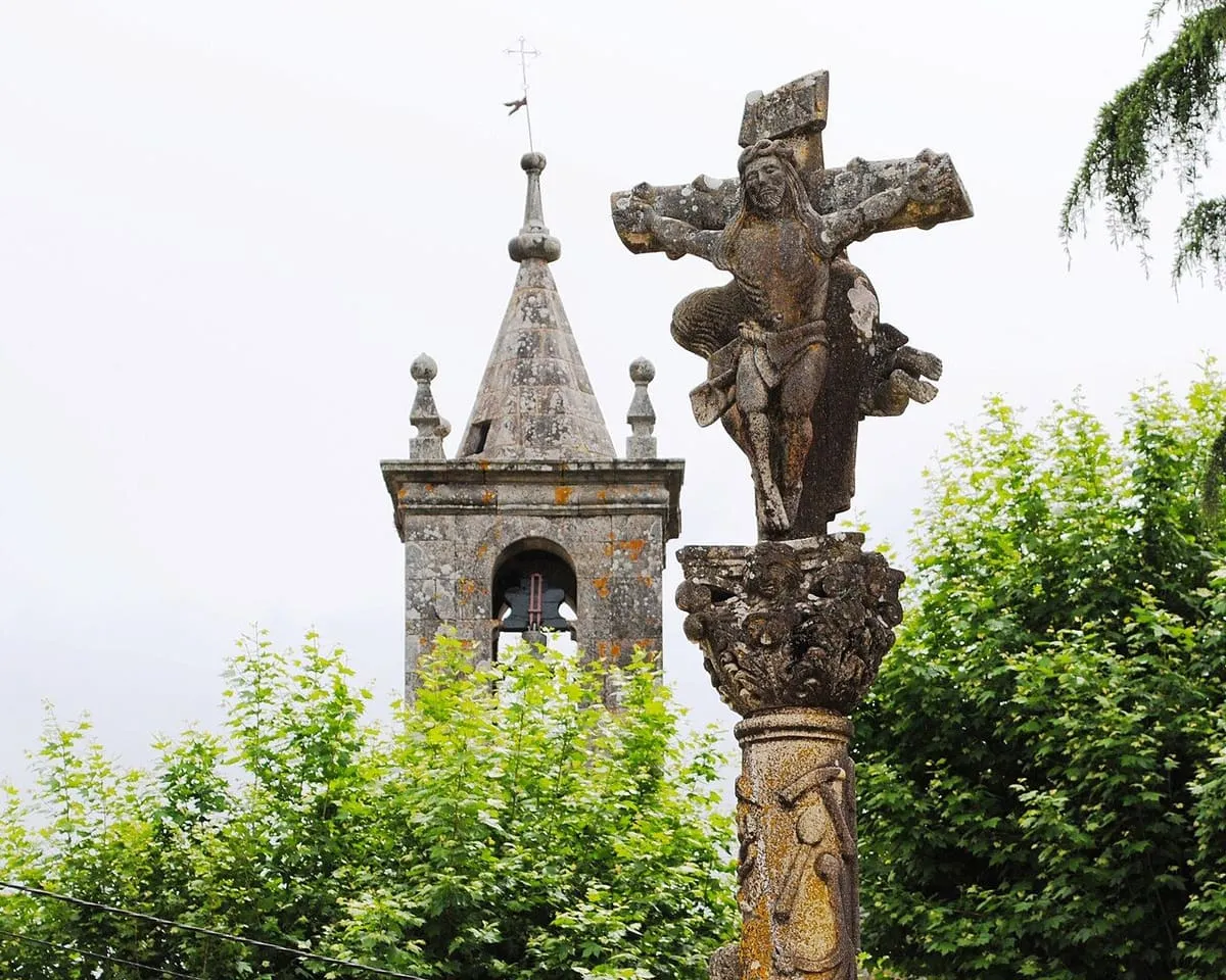 El cruceiro de San Bartolomeu con un Cristo en lo alto, junto al campanario de la iglesia