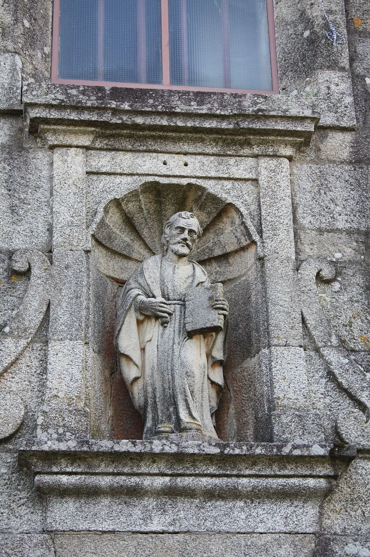 Imagen de un santo con un libro en una hornacina con venera sobre la portada de la iglesia