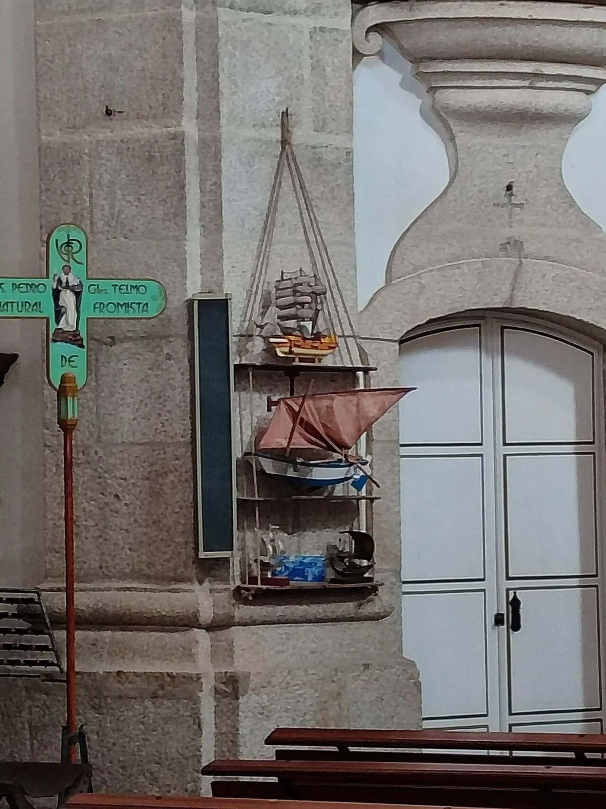Una calle de Tui con un poste que indica San Telmo, una repisa con barquitos y la puerta de la iglesia