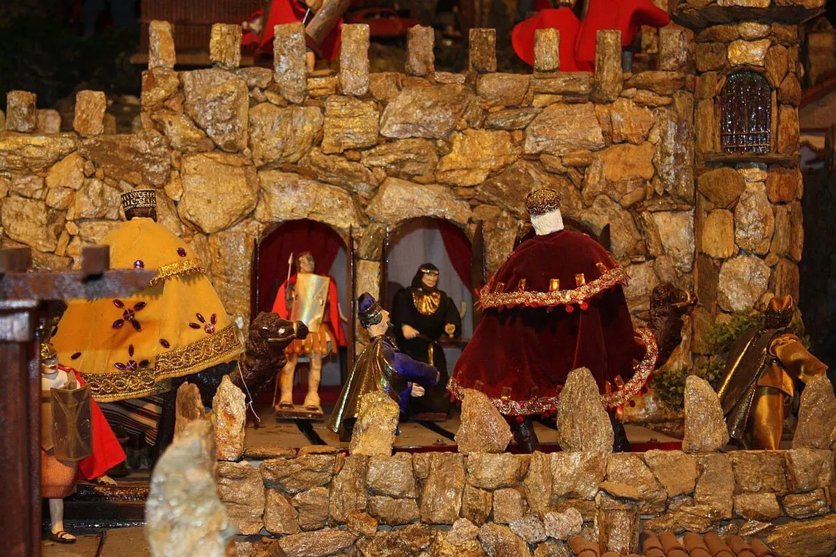 Figuras de Reyes Magos con capas rojas ante un muro de piedra con hornacinas, en el Belén de Valga