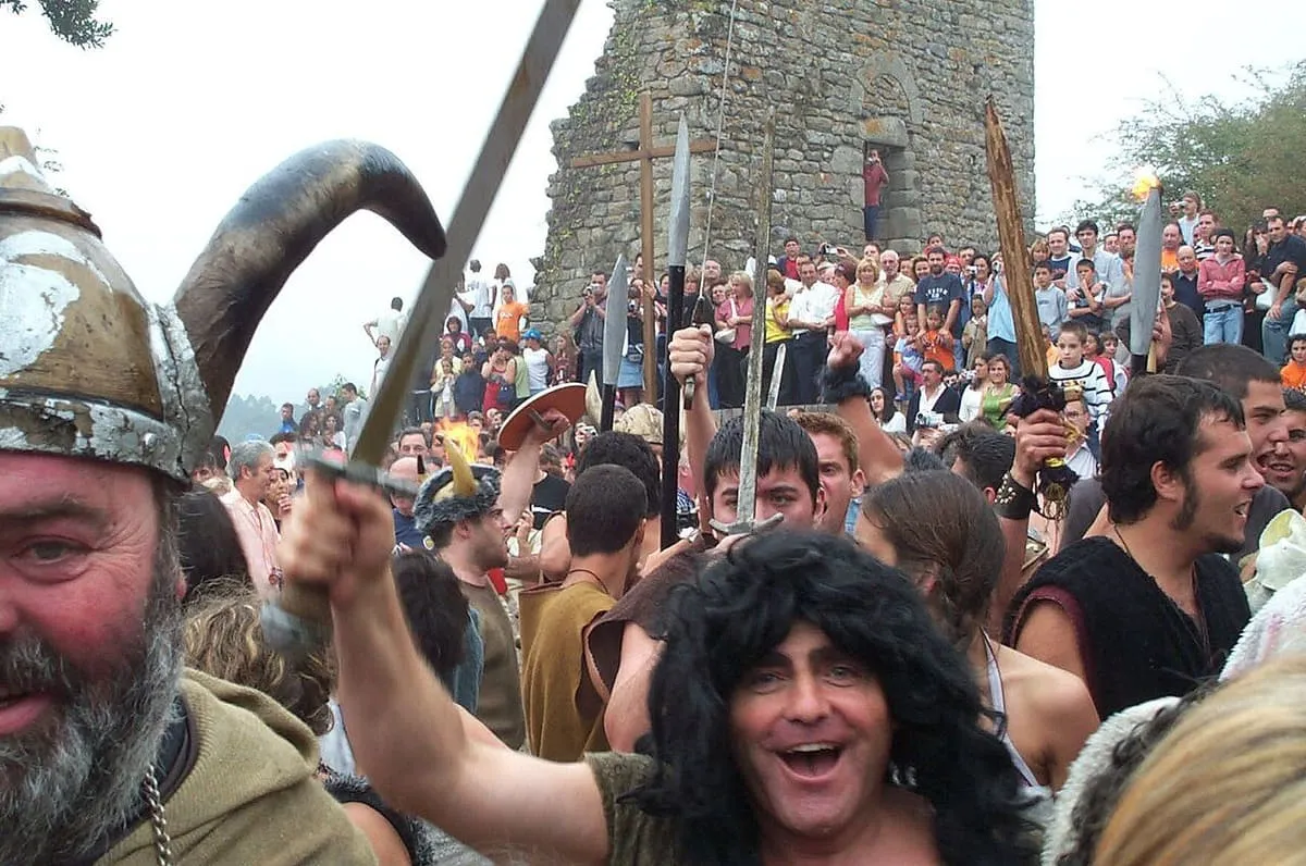Participantes disfrazados de vikingos con cascos y armas entre la multitud, con una de las torres al fondo