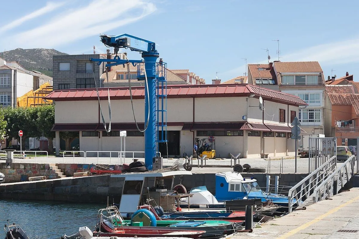 La lonja y el puerto de O Carril, con una grúa azul y barcos amarrados