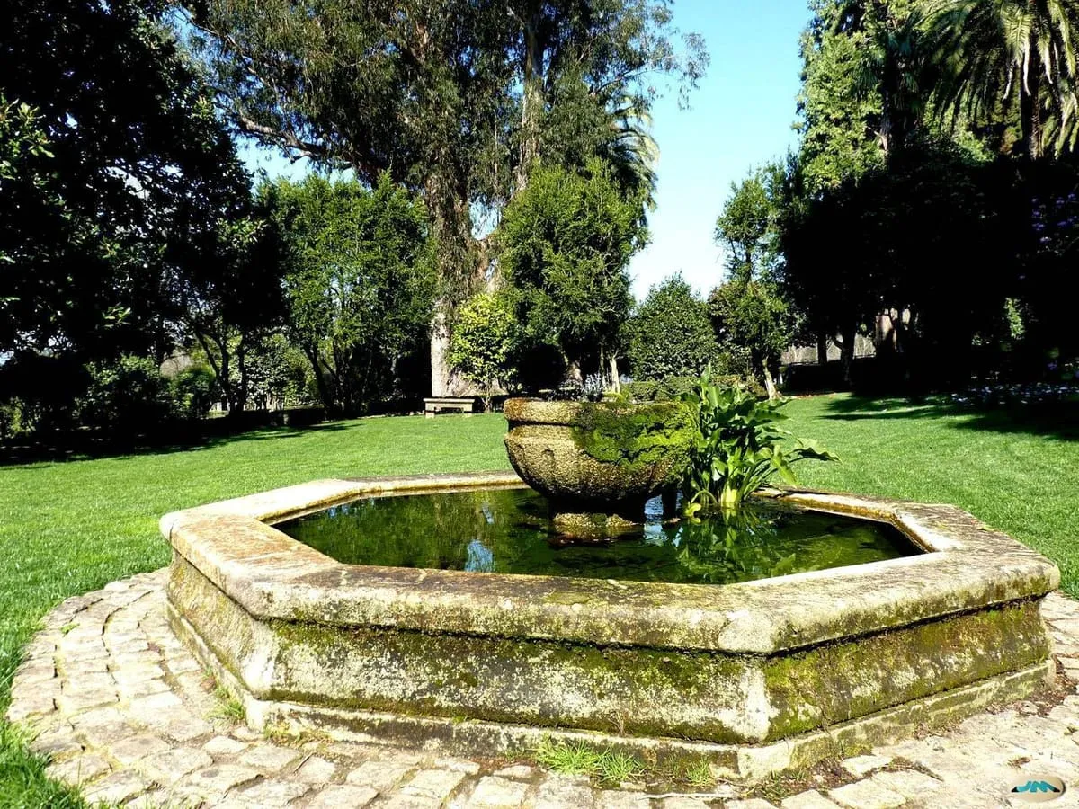 Fuente octogonal de piedra en un jardín de césped con árboles centenarios en el pazo de Rubiáns