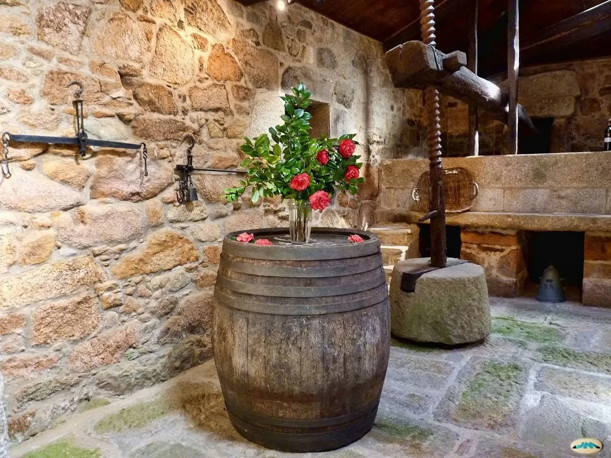 Antiguo lagar de piedra con una prensa de madera y un barril en la bodega del pazo