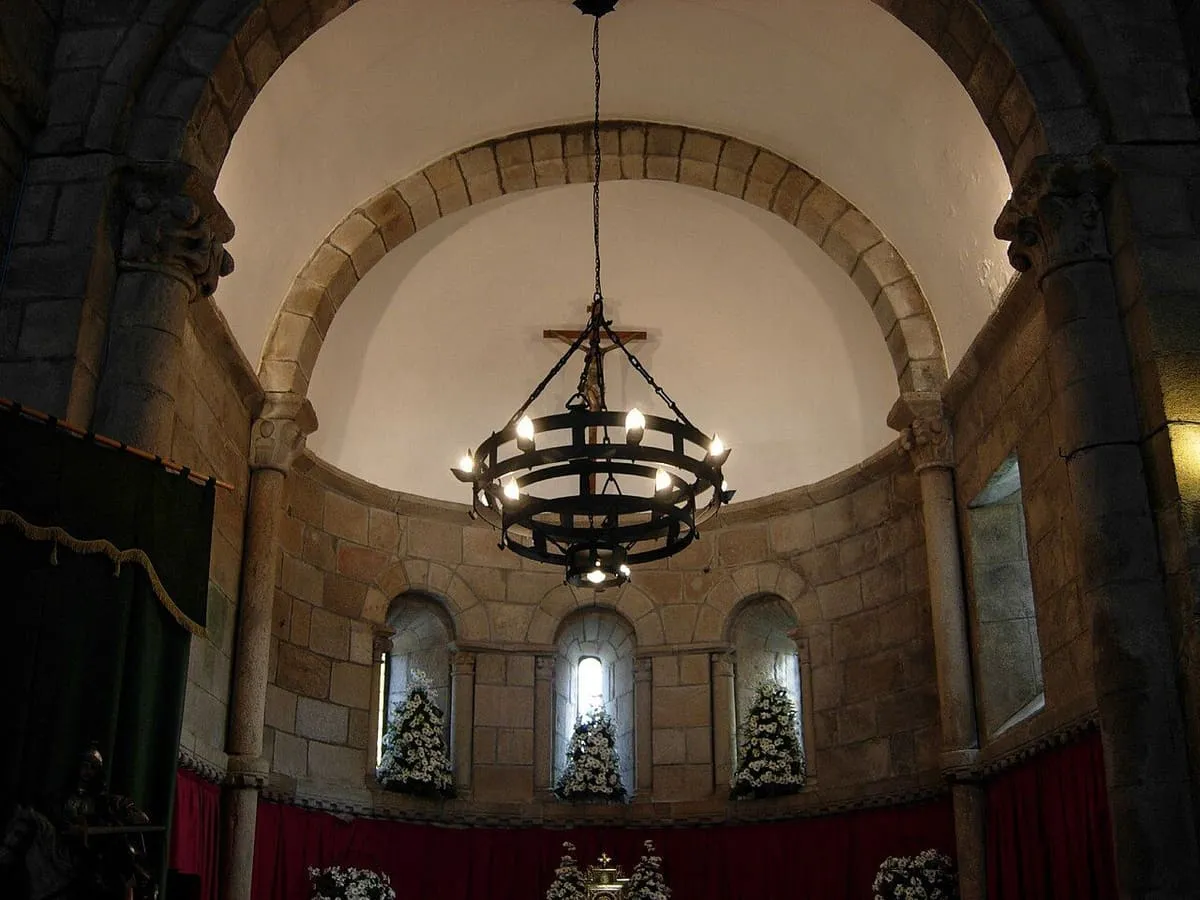Interior del ábside semicircular de Sobrán, con tres ventanas y una lámpara de forja