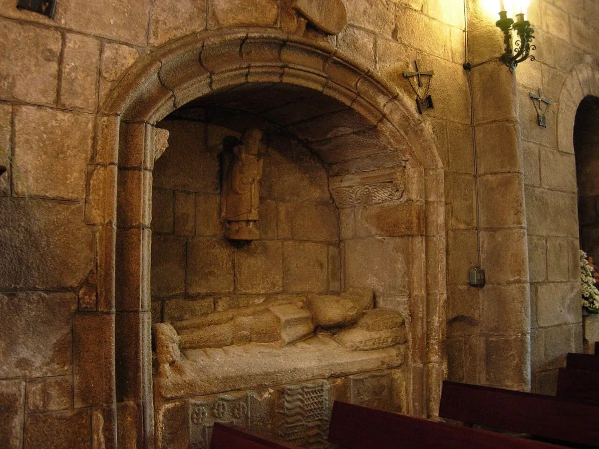 Sepulcro medieval con una figura yacente en un nicho de arco de piedra, dentro de la iglesia