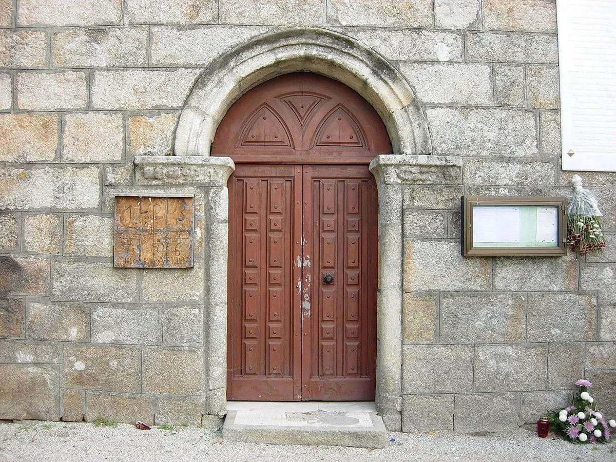 Puerta de arco de medio punto con hojas de madera en un muro de sillares de la iglesia de Caleiro