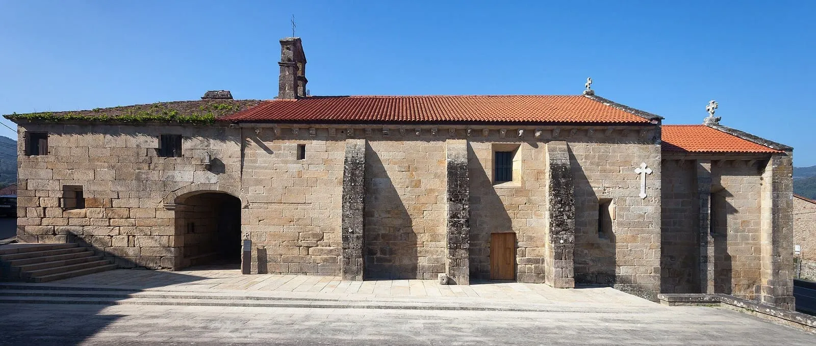 El santuario gótico de la Virxe do Camiño con su tejado rojo y un porche de piedra a la izquierda