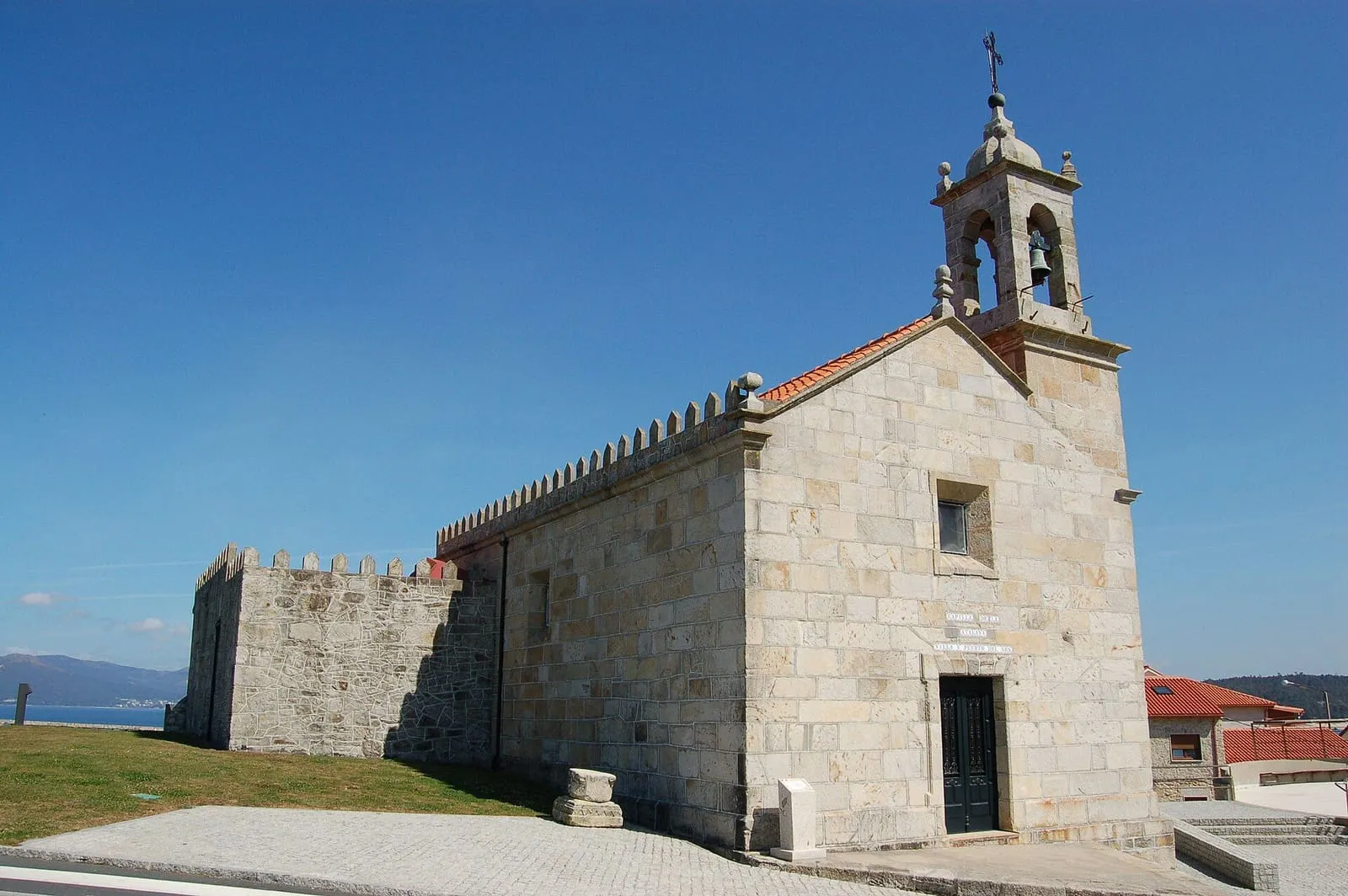 La capela da Atalaia, una ermita de piedra con espadaña junto a un muro almenado y el mar al fondo
