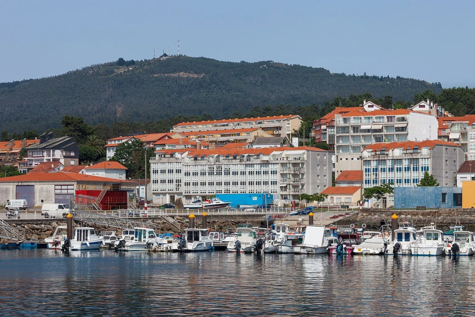 Portosín visto desde el puerto, con casas de tejado rojo y barcos amarrados frente a los montes