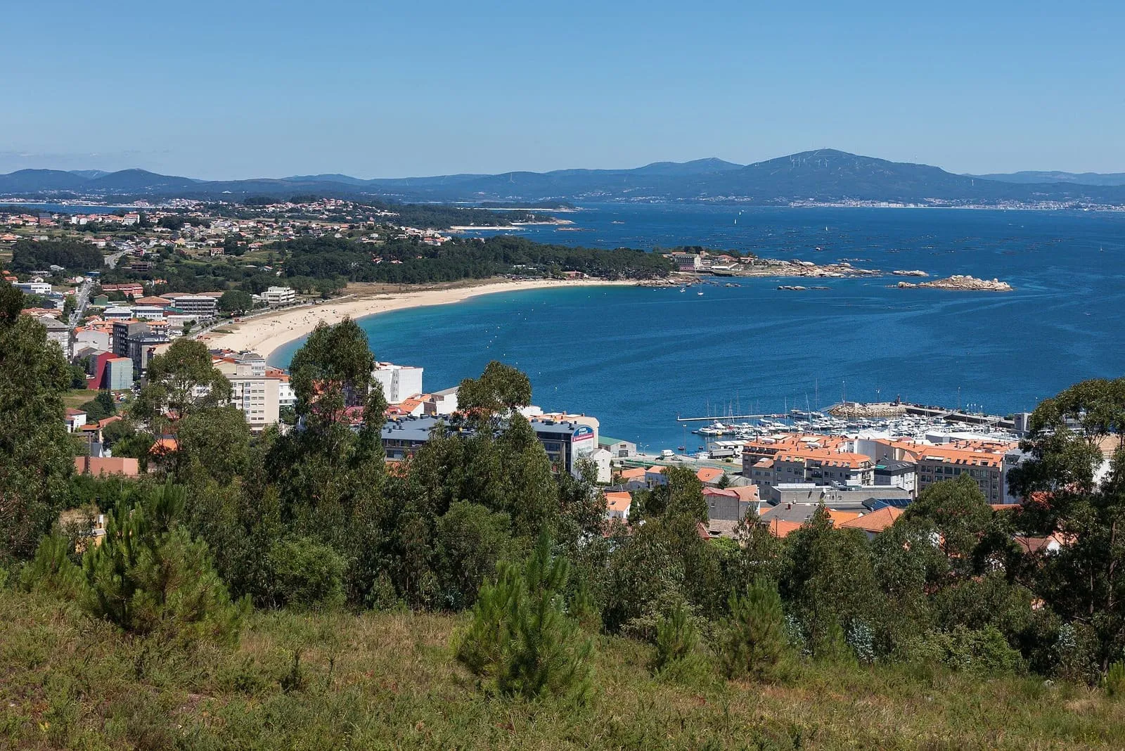 Arenal de Coroso en Ribeira visto desde lo alto, con el puerto deportivo y las montañas al fondo