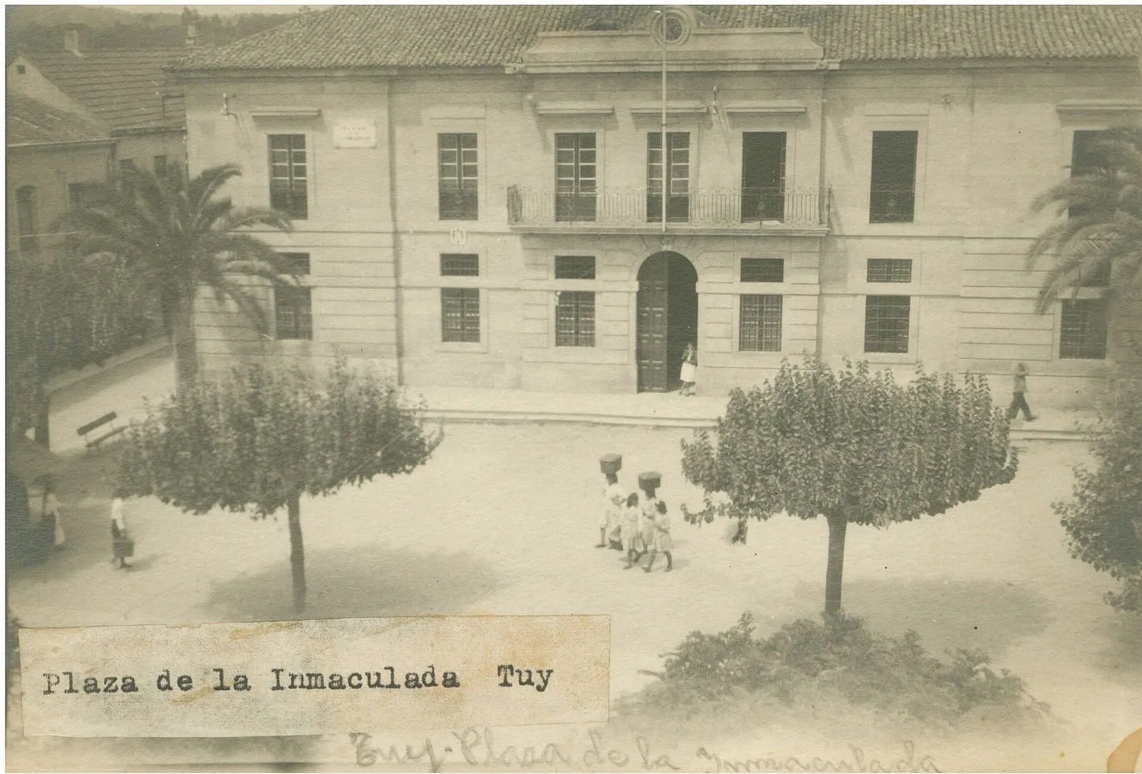 La plaza de la Inmaculada de Tui en una fotografía de 1945, con un edificio de piedra al fondo y dos árboles recortados en primer plano