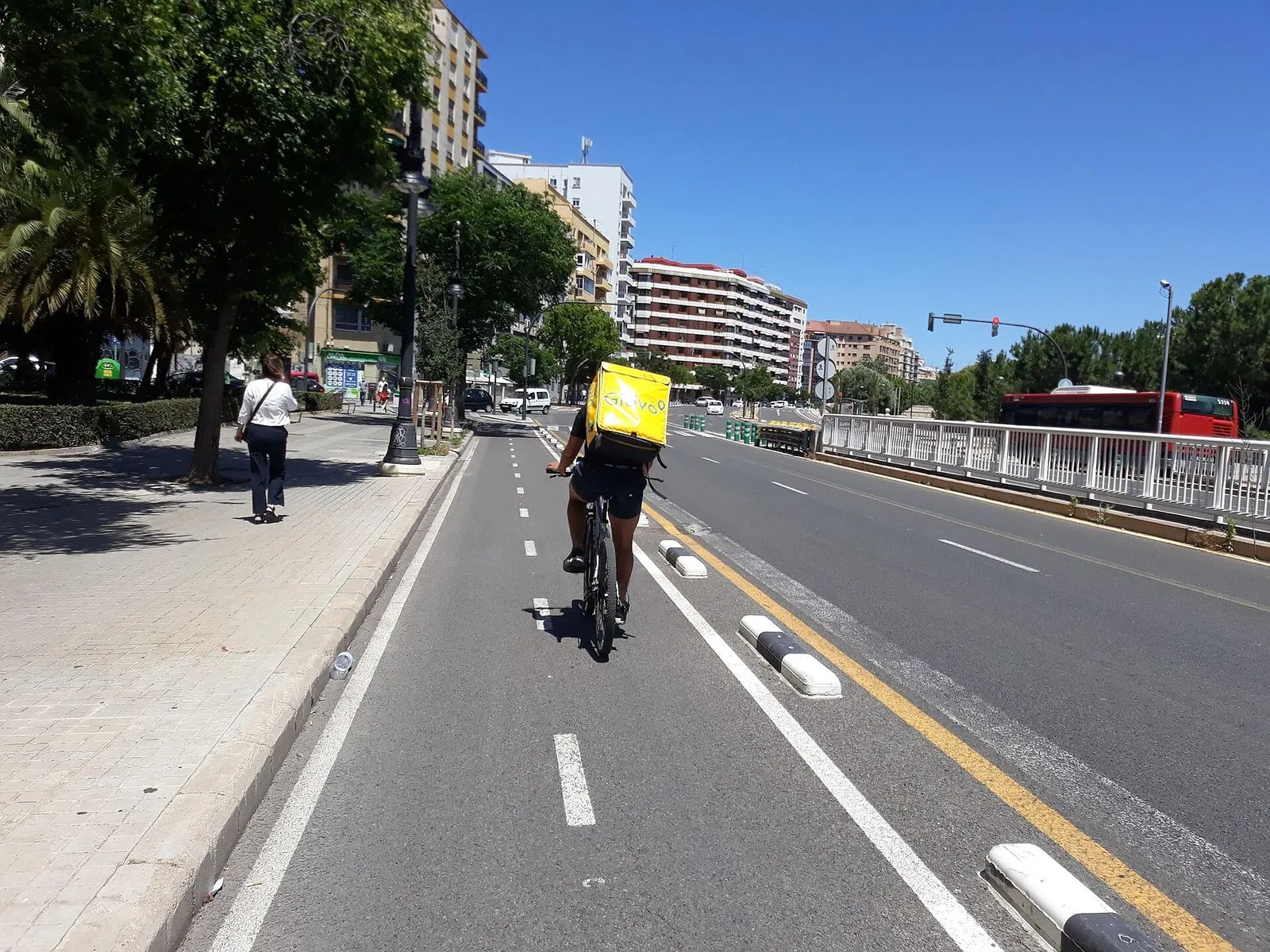 Repartidor de Glovo en bicicleta con la mochila amarilla por un carril bici, imagen de archivo