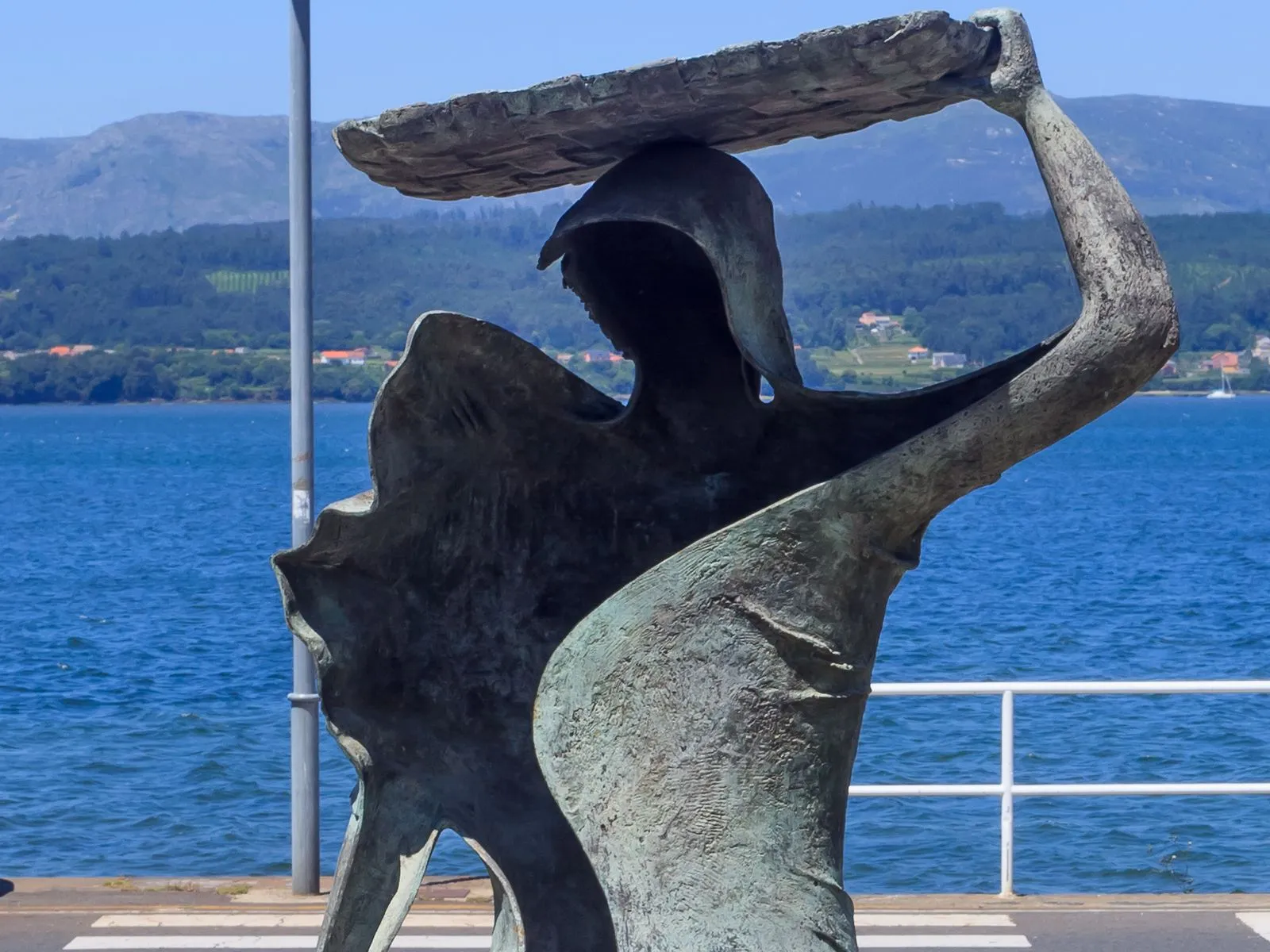 Detalle de la escultura Homenaxe á muller mariscadora, en Rianxo, con una cesta sobre la cabeza y la ría de Arousa al fondo