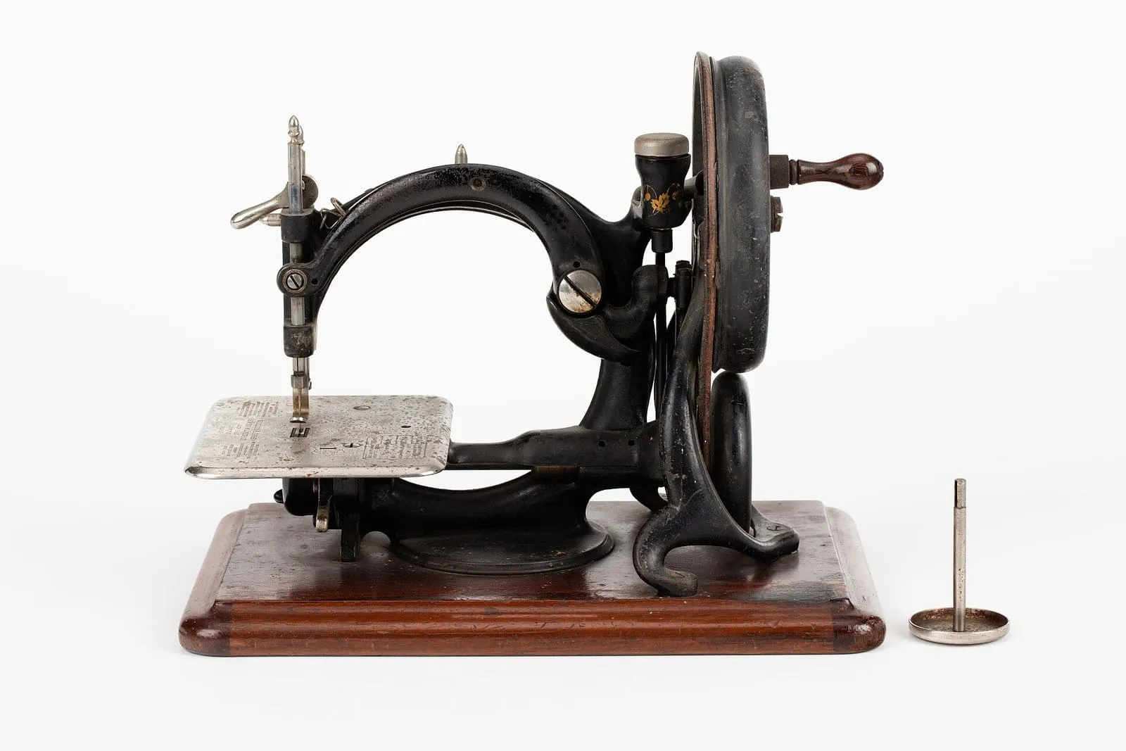 Máquina de coser antigua de manivela, con base de madera y bastidor de hierro negro, sobre fondo blanco