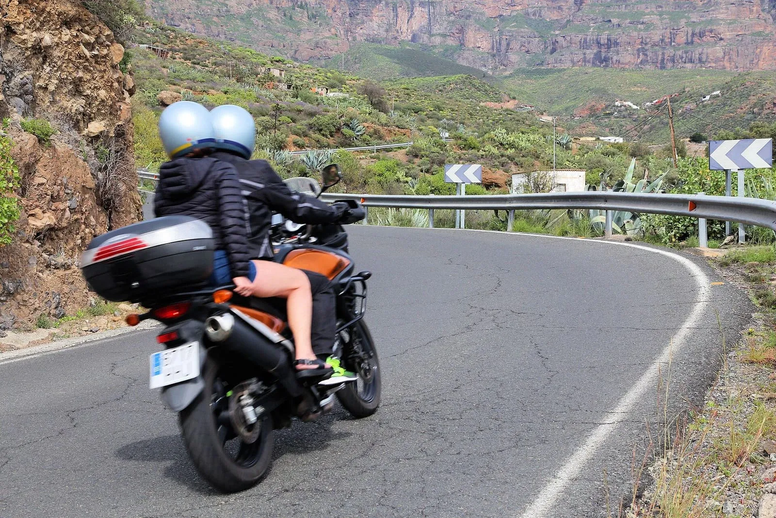 Dos personas en una motocicleta, con casco, tomando una curva de una carretera de montaña