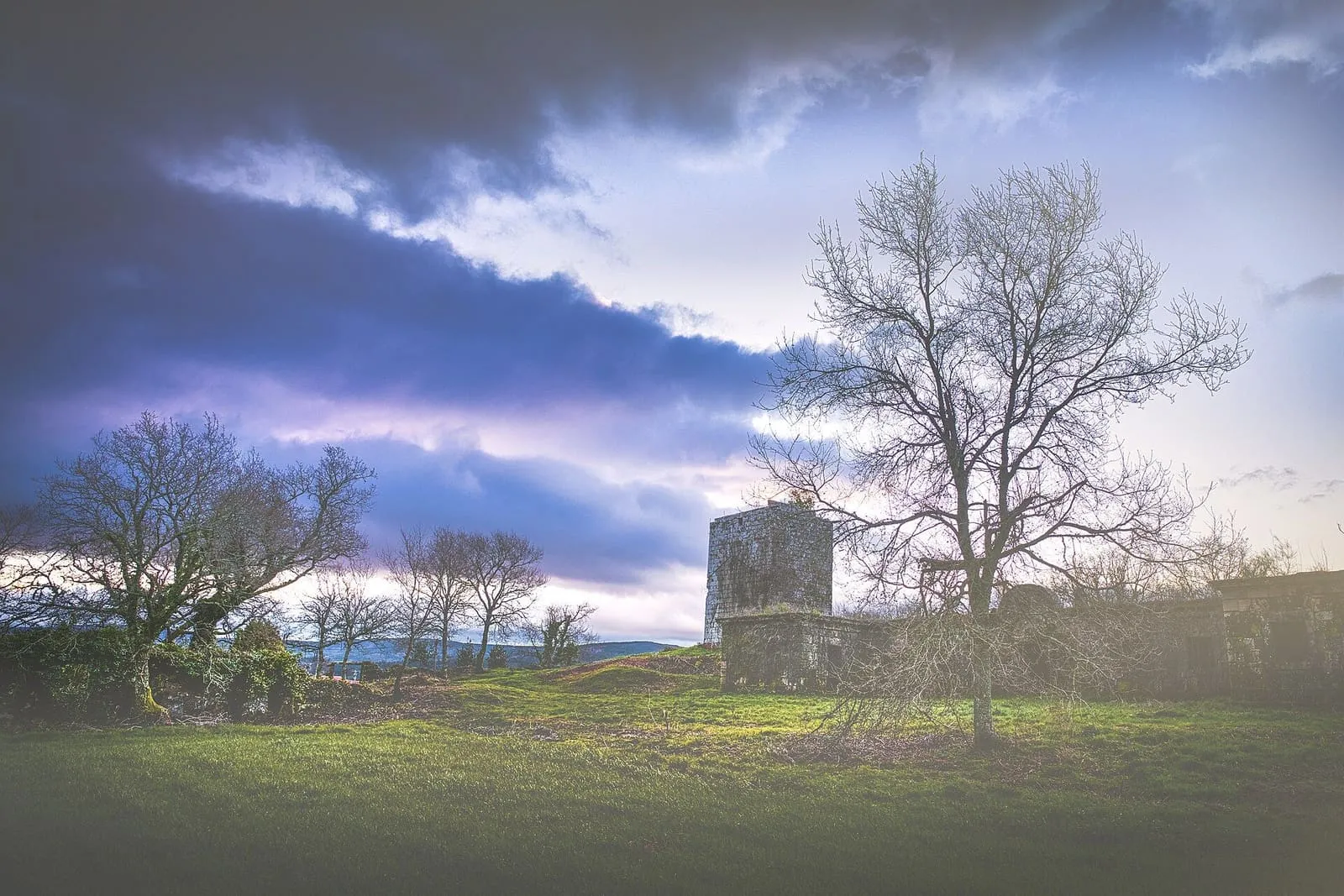 La torre medieval de Guimarei al fondo de un prado, con un cielo nublado de colores