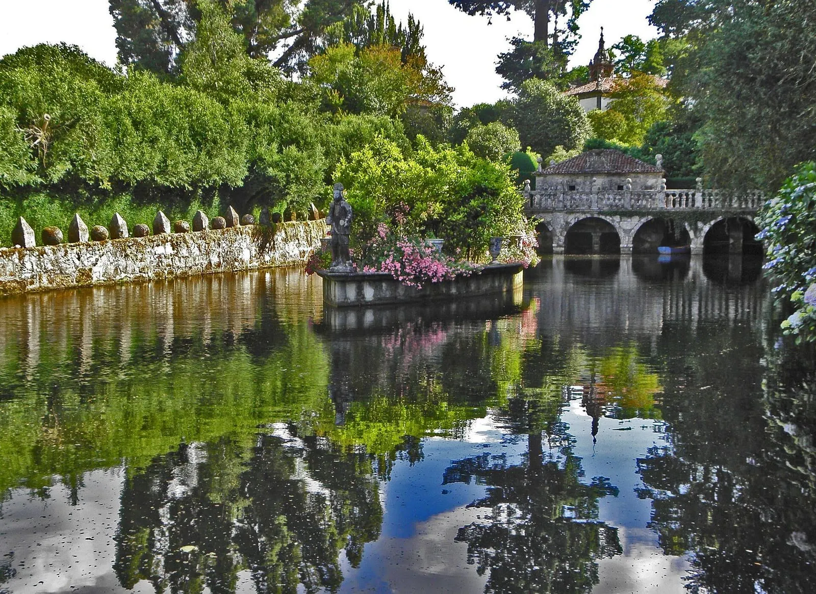 Estanque de los jardines del Pazo de Oca, con un pabellón de arcos y la vegetación reflejada en el agua