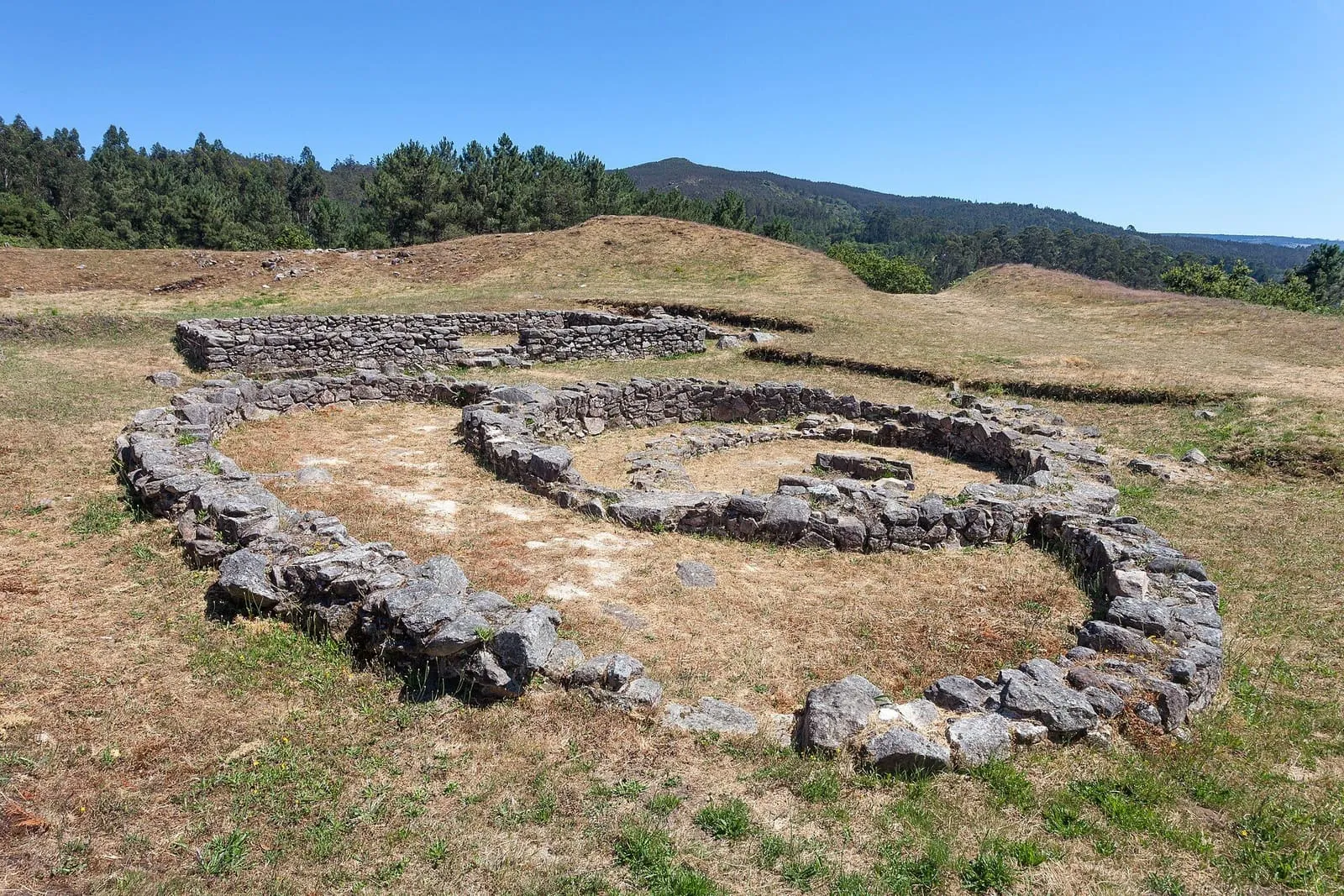 Los cimientos circulares de una casa castreña en el castro de Castrolandín, con una palloza al fondo