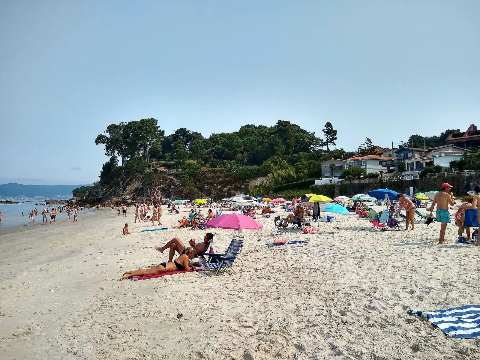 La playa de Lapamán en verano, con sombrillas, bañistas y un arbolado al fondo