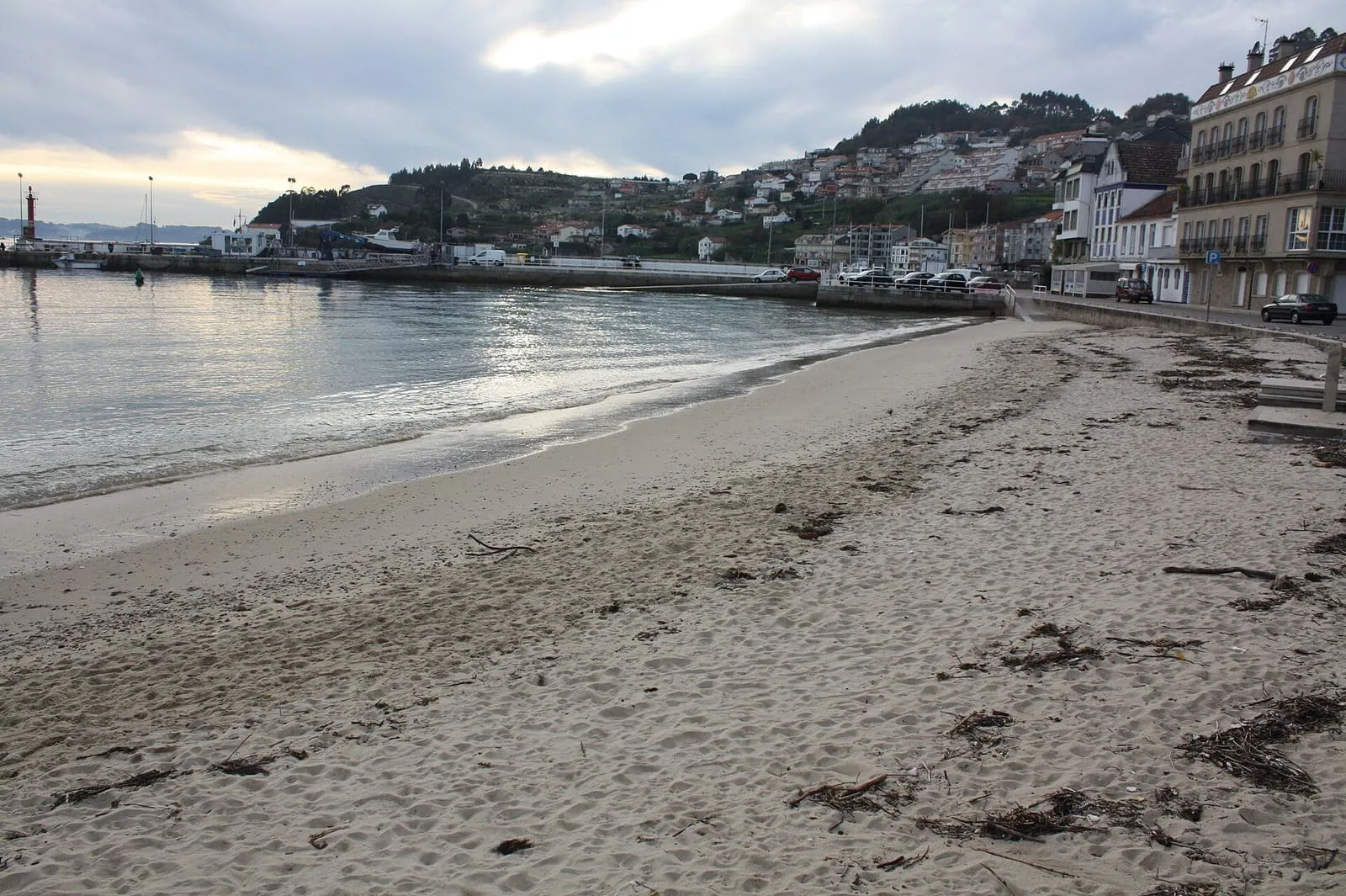 Playa de arena de Raxó junto al puerto y las casas del pueblo
