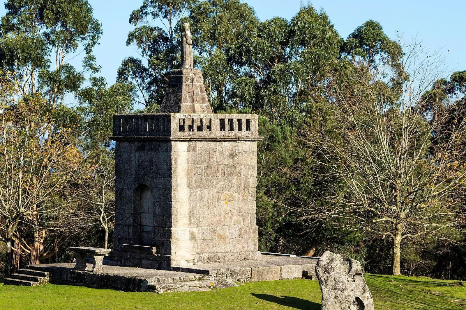 La capilla de Cristo Rei de Xustáns, una pequeña torre cuadrada de piedra con una imagen en lo alto, sobre un monte con hierba