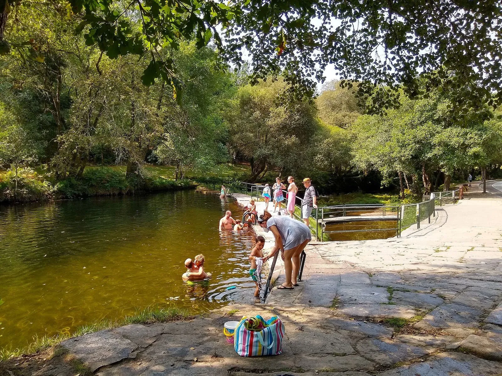 Bañistas en una zona de baño del río Verdugo rodeada de árboles, en A Calzada