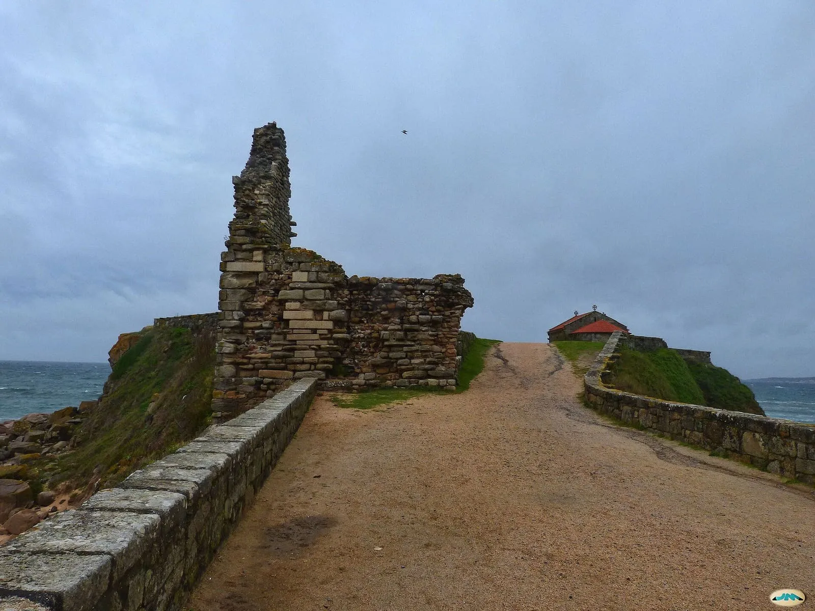Camino de tierra hacia la ermita de la Lanzada, con la pequeña capilla de piedra y el mar al fondo